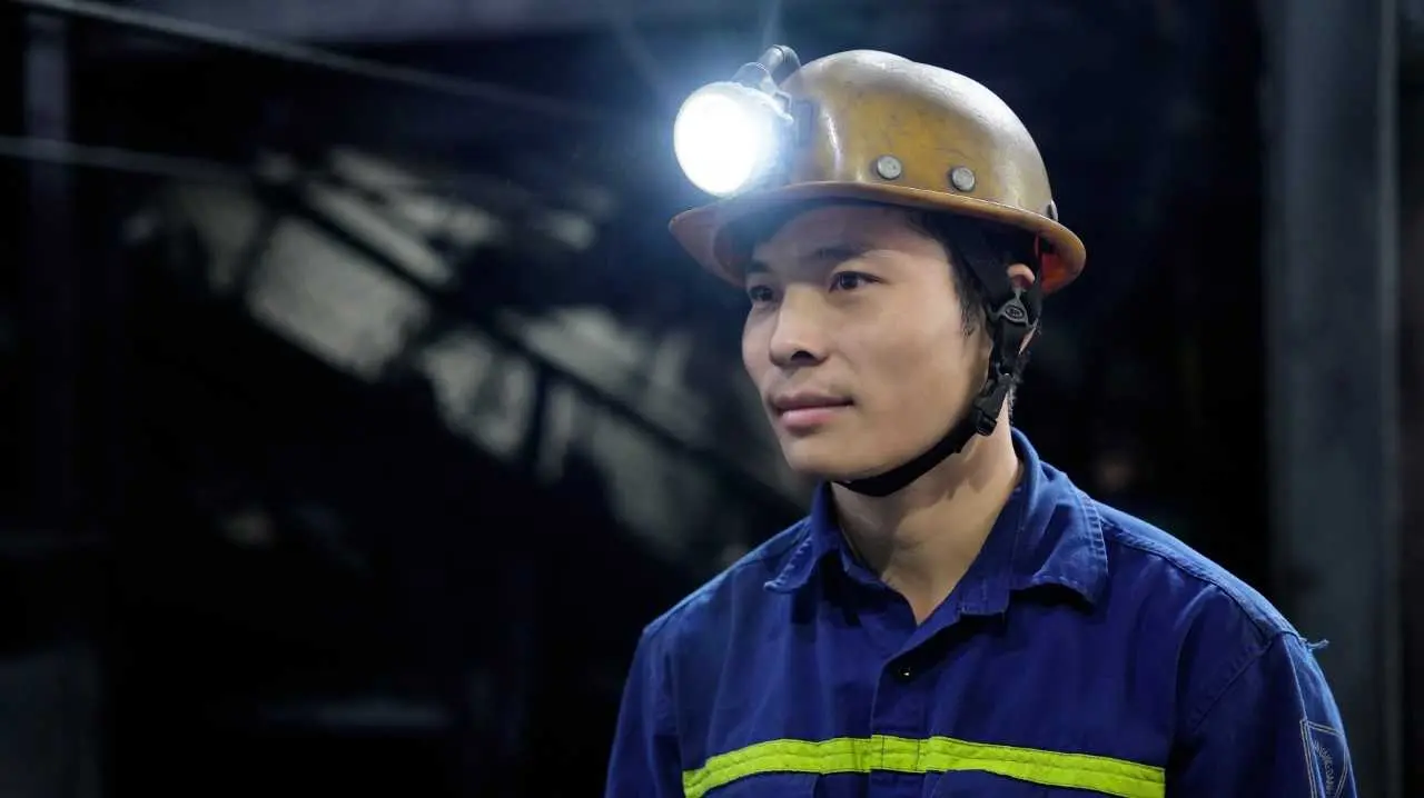 Công nhân trẻ Vinacomin mặc bảo hộ xanh, đội mũ và đèn lò